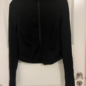 Svart croppad jacka från SHEIN - Säljer en svart croppad jacka från SHEIN med lång ärm och dragkedja framtill. Jackan har en stilren och figurnära passform som ger en snygg siluett. Lululemon doop. Perfekt för dig som gillar minimalistisk och trendig stil. Storlek S passar XS. 