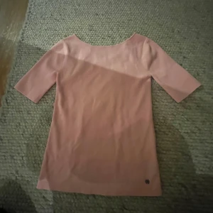 Ljusrosa topp med v-ringning - Säljer en ljusrosa topp med v-ringning på ena sidan och rund hals på andra. Toppen har halvlånga ärmar och är i en mjuk, stretchig bomullsblandning. Enkel och stilren design som passar perfekt till jeans eller kjol.