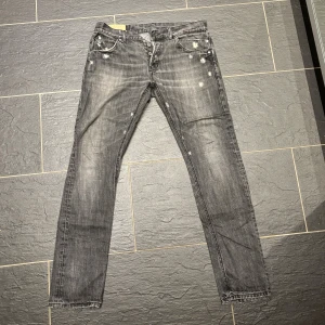 Gråa Dondup jeans med slitningar och detaljer - Snygga grå jeans med slitna effekter och små vita detaljer som ger en cool, använd look. Klassisk femficksmodell med knappgylf och raka ben. Perfekt för dig som gillar streetstyle och vill ha en unik touch på outfiten.