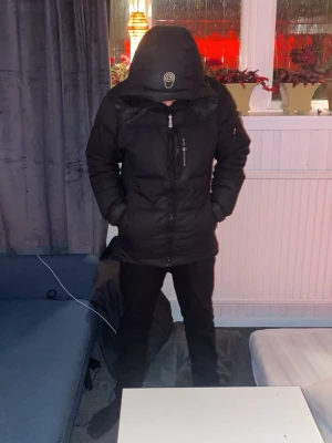 Svart pufferjacka från sailracing  - Säljer en svart pufferjacka från sailracingmed huva och dragkedja framtill. Jackan har en stilren look och är perfekt för kalla dagar. Fylld med syntetmaterial för extra värme och har praktiska fickor på sidorna. Passar dig som gillar streetwear och funktion. Dragkedjan kan man ej dra upp hela vägen