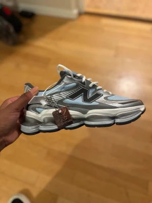 New Balance sneakers i blå och silver - Säljer ett par New Balance sneakers med chunky sula och cool design i blått, silver och svart. Skorna har vit snörning, mesh- och syntetmaterial samt en stor N-logga på sidan. Perfekta för dig som gillar sportig stil och vill sticka ut med dina kicks.