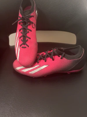 Fotbollsskor - Säljer ett par snygga rosa Adidas fotbollsskor med svarta och vita detaljer. Skorna har klassisk snörning, låg profil och är tillverkade i syntetmaterial för bästa känsla på planen. Perfekta för dig som vill sticka ut på matchen!