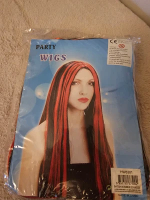 Svart och röd peruk med långa slingor - Säljer en lång peruk i svart med röda slingor, perfekt för party eller maskerad. Peruken har raka längder och är tillverkad i syntetmaterial. Kommer i originalförpackning och är enkel att använda för att skapa en cool look.