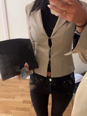 Beige kavaj med silverknäppning - Snygg beige kavaj med figurnära passform och två silverfärgade knäppningar framtill. Jackan har klassisk krage och lång ärm, perfekt för en clean och stilren look. Materialet känns mjukt och har en lätt struktur. Passar dig som gillar minimalistisk stil.