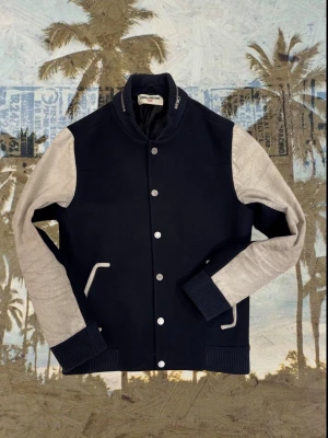 Blå och vit Zadig & Voltaire jacka⚡️ - Snygg bomberjacka från Zadig & Voltaire med mörkblå kropp och ljusgrå ärmar. Jackan har ribbade muddar, silverfärgade knappar och en cool detalj med dragkedja på kragen. Perfekt för dig som vill ha en stilren och modern look.