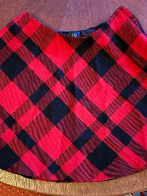 Rutig röd kjol från Polo Ralph Lauren barnstorlek - Säljer en kort kjol från Polo Ralph Lauren med klassiskt röd och svart rutigt mönster. Kjolen är gjord i mjuk manchester och har en snygg A-linjeformad siluett. 