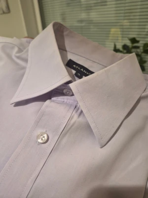 Ljuslila skjorta från Atlant XL - Snygg ljuslila skjorta från Atlant i storlek XL. Klassisk modell med lång ärm, bröstficka och knappar framtill samt vid manschetten. Skjortan är gjord i mjuk bomull och har en stilren, normal passform som funkar till många olika looks.