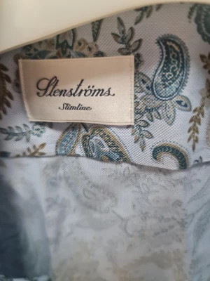 Slimline paisleymönstrad skjorta Stenströms - Snygg slimline skjorta från Stenströms med paisleymönster i blått och brunt på vit botten. Skjortan har klassisk krage, långa ärmar och knappar framtill samt vid manschetten. Tillverkad i mjuk bomull som känns skön mot huden.