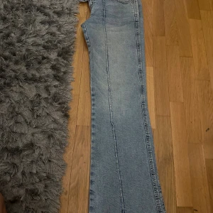 Bootcut jeans från 157 i ljusblå denim - Säljer ett par ljusblå bootcut jeans från 157 med klassisk femficksdesign och hög midja. Jeansen har raka ben som blir vidare nedtill och är tillverkade i mjuk denim. Snyggt läderpatch med 157-logga bak i midjan. Perfekta för dig som gillar retrovibbar och relaxed stil.
