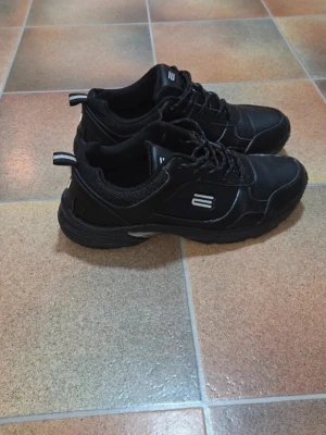 Svarta Promenadskor i Äkta Skinn, Använda 1 gång, Stl 39 - Svarta, bekväma och robusta promenadskor i äkta skinn. Dessa skor är perfekta för vardagsbruk, långa promenader eller för arbete där du står mycket.  Skick: Helt nyskick - Endast använda vid ett enda tillfälle. Sulorna är helt intakta (se bilder). Storlek: Storlek 39.  Material: Ovandel i äkta skinn (Läder). Färg: Helt svart med en diskret silverdetalj på hälen och reflexer / reflekterande remsa baktill.