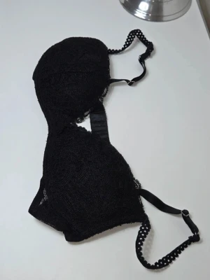 Svart Push Up BH med Fina Spetsdetaljer | Storlek 75C - Klassisk och elegant svart push up-BH i storlek 75C.  Design & Detaljer: Täckt av fin spets. Unika axelband med vågiga/små håldetaljer (picot-kant). Storlek: 75C. Skick: Mycket bra skick