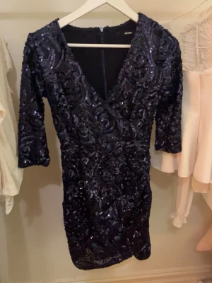 Svart glittrig kortklänning Bik Bok XS - Supersnygg svart kortklänning från Bik Bok i storlek XS. Klänningen har trekvartsärm, v-ringning och är täckt av glittriga paljetter i ett swirl-mönster. Perfekt för dig som vill sticka ut och glänsa! Dragkedja bak för enkel påklädning.