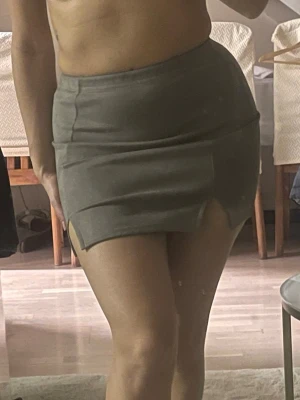 Brun/Grå kortkjol med slitsar - Säljer en grå kortkjol med två små slitsar framtill. Kjolen har en tight passform och är gjord i ett mjukt syntetmaterial som känns skönt mot huden. Enkel och stilren design som är lätt att matcha med olika toppar. Perfekt för dig som gillar minimalistisk stil. Finns ett rivmärken på baksidan se bild nr5