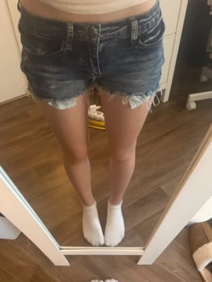 Blå jeansshorts med broderad ficka Str XS - Säljer ett par blå jeansshorts med råa, fransiga kanter och snyggt broderad bakficka med hjärtinspirerat mönster. Shortsen har normal passform och klassisk femficksdesign. Super snygga💕