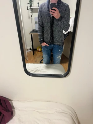 Grå stickad kofta med krage - Säljer en grå stickad kofta med bred krage och svarta detaljer längs knäppningen. Koftan har ribbade muddar vid ärmslut och nederkant, samt långärmad design som passar perfekt för alla dagar. Enkel och stilren look som funkar till jeans.