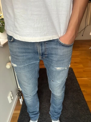 Nudie Jeans  - Säljer ett par jeans med slitningar från Nudie Jeans i modellen Lean Dean. Om det är någon slitning man inte gillar går det att ta bort helt gratis i en nudie butik.   🧵Material: Bomull  📐Storlek: W32 L34 🎅 Modell: Modellen på bilden är 187 cm Perfekt för en stilig look. 🎨 Färg: Ljusblå  ‼️Skickas samma dag eller dagen efter köpet genomförs‼️