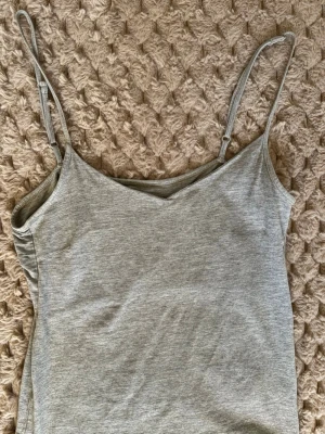 Grå linnetopp från 157 - Säljer en enkel och stilren grå linnetopp från 157 i storlek M. Toppen har smala justerbara axelband och är tillverkad i en mjuk blandning av bomull, viskos och polyester. Perfekt för varma dagar eller som lager under andra plagg.