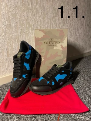 Valentino Garavani Rockrunner sneakers - Säljer ett par Valentino Garavani Rockrunner sneakers i svart och blått med coolt camouflage-mönster. Skorna har snörning, rund tå och detaljer i både mocka och skinn. Perfekta för dig som vill sticka ut med en lyxig streetwear vibe.