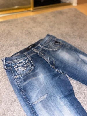 Replay Anbass jeans - Säljer ett par Replay Anbass jeans i blå tvätt med slitningar och snygga detaljer på fickorna. Modellen är skinny med låg midja och klassisk femficksdesign. Jeansen har dragkedja och är gjorda i stretchig bomull för skön passform.