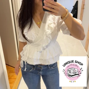 Vit omlottblus med volanger - Säljer en söt vit omlottblus med volanger och spetsdetaljer. Blusen har korta puffärmar, knyt i sidan och v-ringad hals. Materialet känns lätt och luftigt, perfekt för ljusa dagar. Passar dig som gillar romantisk och feminin stil.