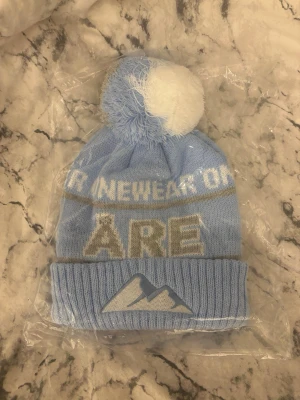 Åre mössa - Snygg ljusblå stickad mössa med vit och grå tofs på toppen.