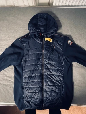 Svart pufferjacka från Parajumpers - Svart pufferjacka från Parajumpers med huva, quiltad framsida och ärmar i mjukare material. Jackan har dragkedja, bröstficka med dragkedja och klassisk Parajumpers-patch på ärmen. Perfekt för kyliga dagar och snygg streetstil. Står att det är large men tror att det är i junior eftersom jag köpte den i tyskland, den är lite stor på mig är 175 väger 75. Helst inte byten men kan tänka på saken om budet är jättebra. Ni är mer än välkomna att skriva:)
