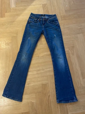 Blå bootcut jeans från LTB W25 L30 - Snygga blå jeans från LTB med bootcut passform och klassisk femficksdesign. Jeansen har en mörkblå tvätt med lätt slitna detaljer och kontrastsömmar. Tillverkade i Turkiet och gjorda i jeansmaterial. Perfekta för dig som gillar en lite vidare benform.