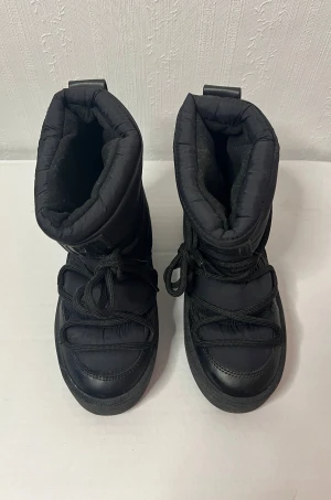 Svarta moon boots med snörning H&M  - Säljer ett par svarta moon boots med tjock vaddering och snörning framtill. Skorna har en platt sula och är till soppa i syntetmaterial, perfekta för kalla vinterdagar. Supersköna men använt en gång och blivit ståendes tyvärr