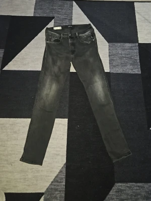 Replay Anbass svarta slim jeans - Svarta Replay Anbass jeans i slim fit med snygga slitningar och klassisk femficksdesign. Jeansen har en smal passform och är tillverkade i stretchigt Hyperflex-material för extra komfort. Perfekt för dig som gillar en modern och stilren look.