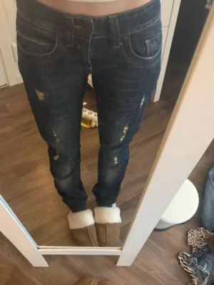 Mörkblå jeans med slitningar Str XS - Säljer ett par mörkblå jeans med snygga slitningar på benen och detaljerade sömmar. Jeansen har klassisk femficksdesign och raka ben. Materialet är robust denim och passformen är normal. Snygga💕