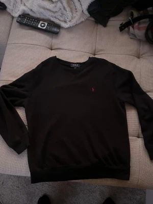 Svart tröja från Polo Ralph Lauren - Svart långärmad tröja från Polo Ralph Lauren med klassisk rund hals och röd broderad logga på bröstet. Tröjan har en enkel och stilren . Perfekt för dig som behöver en snygg tröja till vintern.