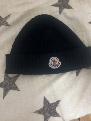 Moncler Mössa (Äkta) - Detaljer .kolsvart jungfruullblandning ribbstickad logotypmärke framtill stretchig design vikt kant.  Köpte den i London, 2024.December för 2300