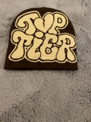 Mössa - Brun mössa med text där det står ”top tier”. Kan eventuellt tänka mig gå ner i pris