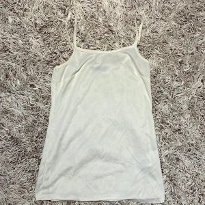 Vit linne från Kids By Lindex - Säljer en enkel och stilren vit linne från Lindex med smala justerbara axelband. Linnet har en rak passform, tillverkad i mjuk och lätt polyester. Perfekt för dig som gillar minimalistisk stil och vill ha något bekvämt och luftigt.  Den har några skador (se bilderna) Storlek EUR 158/164 för 12-14 år