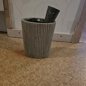 Grå kruka med batteridrivna ljus - Bilderna visar en grå kruka i keramik struktur och två  metallkoner med dekorativa hål, samt batteridrivna ljus