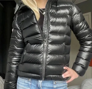 Svart dunjacka från colmar - Kan sänka enda till 2500! Pls buy!!❤️ Säljer en svart, glansig dunjacka från colmar med huva och tvåvägsdragkedja. Jackan har quiltad design, lång ärm och logotyp på ärmen. Perfekt för kalla dagar och har en snygg, modern look som funkar till jeans och sneakers.