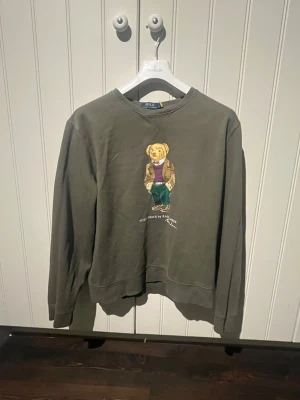 Grå sweatshirt från Polo Ralph Lauren - Säljer en grå sweatshirt från Polo Ralph Lauren i storlek L. Tröjan har ett klassiskt björntryck på bröstet och rund hals. Långärmad och tillverkad i mjuk bomull, perfekt för chill dagar. En ikonisk och stilren tröja med relaxed passform.