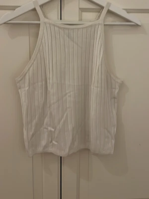 Vit ribbad linnetopp från H&M Divided - Säljer en vit ribbad linnetopp från H&M Divided i storlek M. Toppen har raka axelband och är ärmlös med en snygg, vertikal ribbad struktur. Perfekt för varma dagar och enkel att matcha med jeans eller shorts.