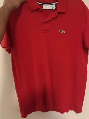 Röd pikétröja från Lacoste - Klassisk röd pikétröja från Lacoste med korta ärmar och krage. 