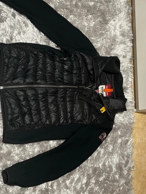 Svart dunväst Parajumpers Warm Up M - Säljer en svart cardigan från Parajumpers i modellen Warm Up, storlek M. Västen har quiltad framsida, dragkedja och en ikonisk gul detalj vid kragen. Perfekt för våren och i helt nyskick😮‍💨
