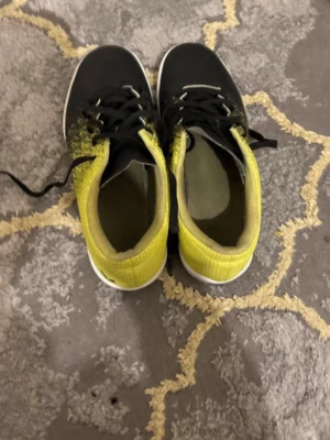 Svarta och gula sneakers från EDC - Säljer ett par snygga sneakers från EDC i storlek 36. Skorna är svarta framtill och övergår i gult mot hälen, med coolt prickigt mönster. De har svart snörning och vit sula. Ovandelen är i syntetmaterial med meshstruktur för extra komfort.