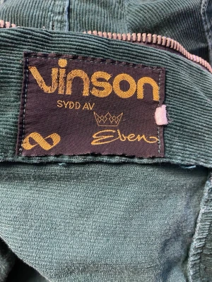 Grön manchesterjacka från Vinson  - Vintage producerad av Eben för Kooperativa förbundet, uppskattad 1970-tal. Säljer en grön manchesterjacka från Vinson med coola dragkedjor på bröstfickorna. Jackan har klassisk krage, långa ärmar och tryckknappar vid ärmsluten. Perfekt för dig som vill sticka ut med en retrovibe och snygg struktur. One-of-a-kind!!! Modellen passar både dam/herr/unisex