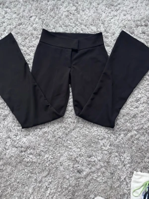 Svarta bootcut kostymbyxor  - Säljer ett par svarta kostymbyxor från Gina Tricot i storlek XS. Byxorna har bootcut-modell med låg midja, diskret bakficka och stängs med hake och dragkedja fram. Materialet är mjukt och stretchigt, vilket gör dem riktigt bekväma.