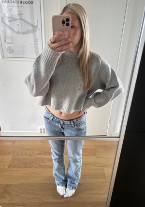 Grå croppad stickad tröja från Zara - Säljer en ljusgrå croppad stickad tröja från Zara. Tröjan har en loose passform, ribbade muddar och är långärmad. Perfekt att slänga på sig till jeans för en chill look.