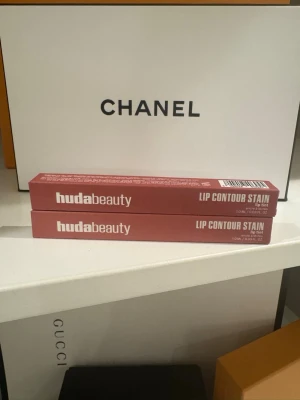 Huda Beauty Lip Contour Stain Rosewood 2-PACK - Säljer två Huda Beauty Lip Contour Stain i färgen Rosewood. Det är en lip tint med en mjuk, rosabrun ton. Produkten är lätt, långvarig och berikad med arganolja för extra vård. Varje förpackning innehåller 1 ml och har en stilren, matt rosa kartong. 2-PACK