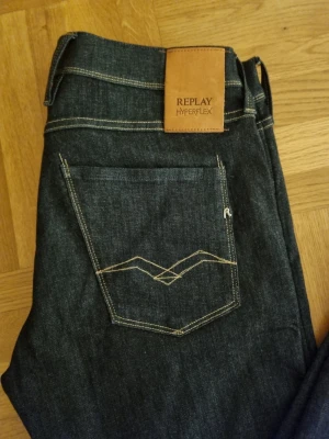 Replay Hyperflex Anbass jeans, blå, W34/L34 - Säljer ett par mörkblå Replay Hyperflex Anbass jeans i slim fit. Klassisk femficksmodell med snygga kontrastsömmar och diskret Replay-logga på bakfickan. Jeansen är tillverkade i stretchigt denim för extra komfort och har en modern, smal passform.