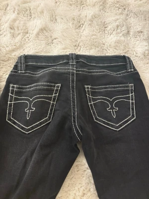 Svarta bootcut jeans - Säljer ett par svarta jeans från Gina Tricot i storlek XS. Jeansen har tydliga vita kontrastsömmar och snygga bakfickor med broderad detalj. Klassisk femficksmodell och normal passform. Perfekta till en cool vardagslook. De är även lågmidjade.