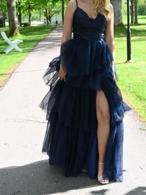 Marinblå balklänning med volanger - Säljer en marinblå balklänning med tunna axelband, banden är även justerbara! Och snörning bak på ryggen så man kan dra åt hur mycket man vill 