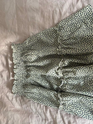 Leopardmönstrad kortkjol från H&M - Säljer en beige kortkjol från H&M med svart leopardmönster. Kjolen har smock i midjan och volangdetaljer som ger en söt och trendig look. Perfekt för dig som gillar djurmönstrat och vill ha något bekvämt och snyggt.