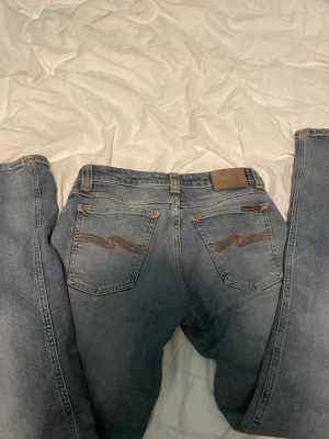 Nudie Jeans blå jeans W29 L32 - Säljer ett par klassiska blå jeans från Nudie Jeans med snygga kontrastsömmar och broderade bakfickor. Modellen har normal passform och raka ben. Tillverkade i slitstarkt bomullsmaterial och har en tidlös look som funkar till allt.